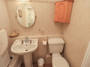 A bathroom with a sink a toilet a round mirror a wooden wall cabinet and a towel on a radiator at Peak View in Keswick