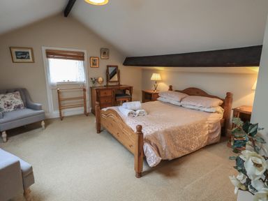 A bedroom with a wooden bed, bedside tables with lamps, a dressing table, armchairs and a window at Peak View in Keswick