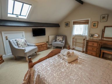 A bedroom with a bed, two armchairs, a wooden dresser with a mirror, a television on the wall, and a skylight window at Peak View in Keswick