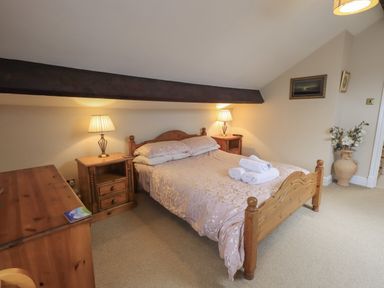 A bedroom with a wooden bed with folded towels on it two bedside tables with lamps and a wooden chest of drawers at Peak View in Keswick