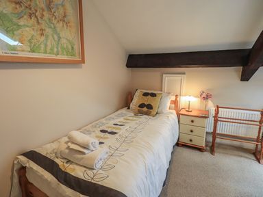 A single bed with folded towels on it next to a small bedside table with a lamp and flowers at Peak View in Keswick