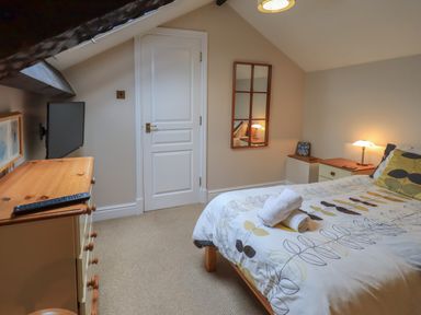 A small bedroom with a bed with patterned bedding a dresser with a remote a wall-mounted TV a door and a mirror on the wall at Peak View in Keswick