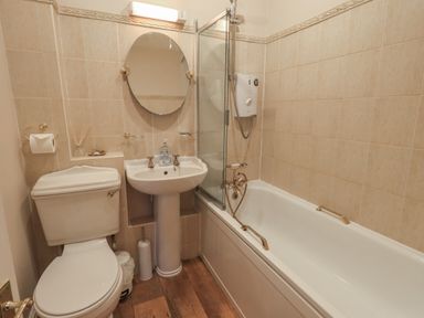 A bathroom with a toilet sink round mirror and bathtub with shower at Peak View in Keswick