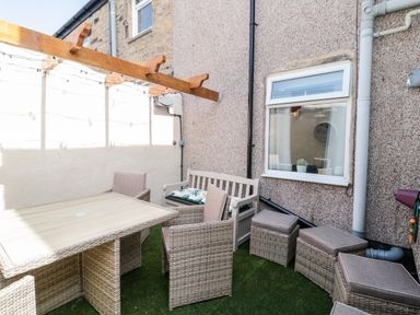 An outdoor patio with a table chairs a bench and ottomans under a wooden pergola at Bonnies Retreat in Amble