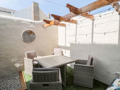 An outdoor patio with a wooden pergola wicker chairs around a table and a circular wall decoration at Bonnies Retreat in Amble