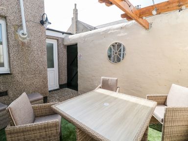 An outdoor patio with a square table and four cushioned wicker chairs under a wooden pergola at Bonnies Retreat in Amble