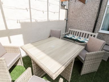 An outdoor seating area with a square table surrounded by four cushioned chairs and a wooden bench with a floral cushion at Bonnies Retreat in Amble