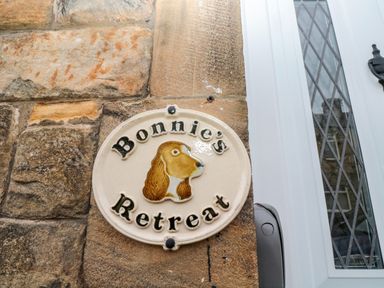 A ceramic sign with a dog's head and the words Bonnies Retreat mounted on a stone wall next to a white door with diamond-patterned glass at Bonnies Retreat in Amble