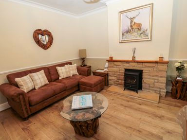 A living room with a brown sofa and plaid pillows a glass coffee table a stone fireplace and a painting of a deer at Bonnies Retreat in Amble