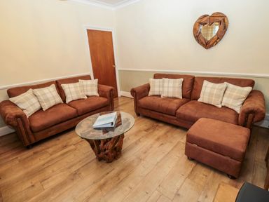 A living room with two brown sofas with cushions a glass coffee table and a wooden heart-shaped wall mirror at Bonnies Retreat in Amble