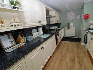 A kitchen with white cabinets black countertops wooden floor and various kitchen appliances at Bonnies Retreat in Amble