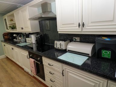A kitchen with white cabinets black countertops an oven toaster bread box and recycling bin at Bonnies Retreat in Amble