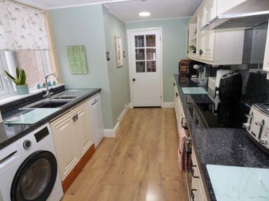 A kitchen with wooden floor black countertops washing machine and dishwasher at Bonnies Retreat in Amble