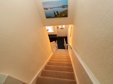 A staircase with beige carpet leading down to a front door with a black mat and a bench nearby at Bonnies Retreat in Amble