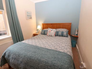 A bedroom with a double bed a wooden headboard bedside table with lamp and curtains at Bonnies Retreat in Amble