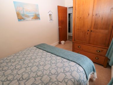 A bedroom with a bed covered in a patterned blanket a wooden wardrobe with drawers an open wooden door and a wall painting at Bonnies Retreat in Amble