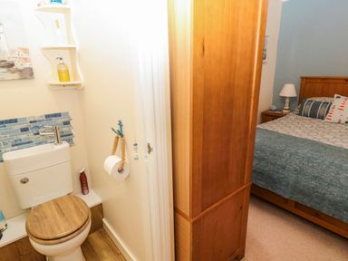 A small bathroom with a toilet and shelf next to a bedroom with a wooden bed and nightstand at Bonnies Retreat in Amble