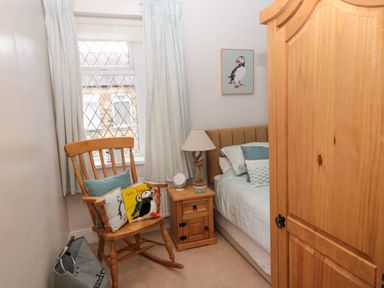 A small bedroom with a wooden rocking chair by a window a wooden bedside table with a lamp a bed with pillows and a wooden wardrobe at Bonnie's Retreat in Amble