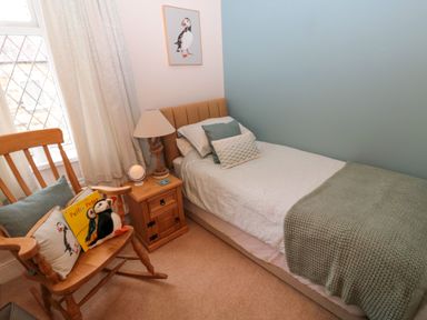 A bedroom with a single bed and a nightstand with a lamp next to a wooden rocking chair with cushions and a stuffed penguin at Bonnies Retreat in Amble