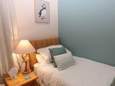 A small bedroom with a single bed a wooden nightstand with a lamp and a small mirror and a framed puffin picture on the wall at Bonnies Retreat in Amble