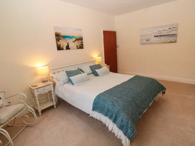 A bedroom with a double bed two bedside tables with lamps chair and two paintings on the walls at Bonnie's Retreat in Amble