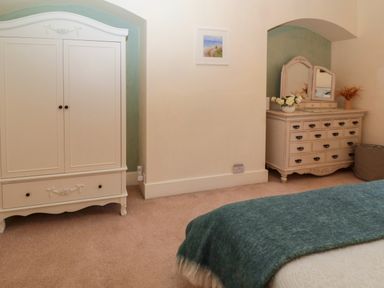 A bedroom with a white wardrobe, a dresser with mirrors and flowers, and a bed with a blue blanket at Bonnies Retreat in Amble