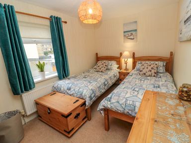 A bedroom with two single beds a wooden chest and a window with teal curtains at Bonnies Retreat in Amble