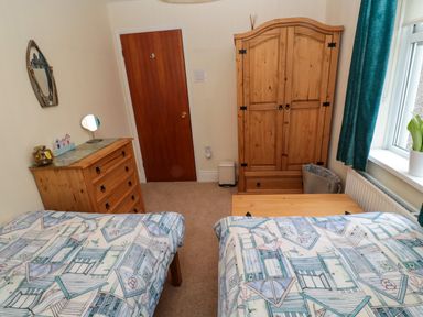 A bedroom with two single beds a wooden wardrobe a chest of drawers a wooden door and a window with a curtain at Bonnie's Retreat in Amble