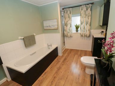 A bathroom with a bathtub a toilet a sink and a shower area with a window and curtains at Bonnies Retreat in Amble