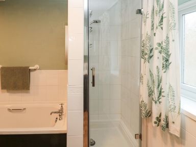 A bathroom with a bathtub a towel rack a glass shower enclosure and a window with a floral curtain at Bonnies Retreat in Amble