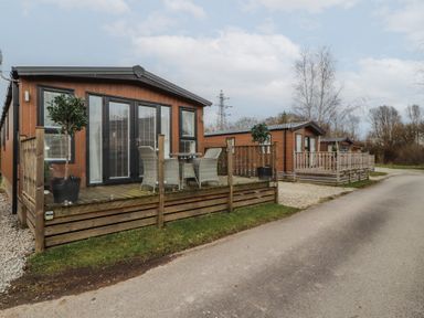 A row of wooden cabins with small fenced porches and outdoor seating along a paved road at 24 Sherwood in Carnforth