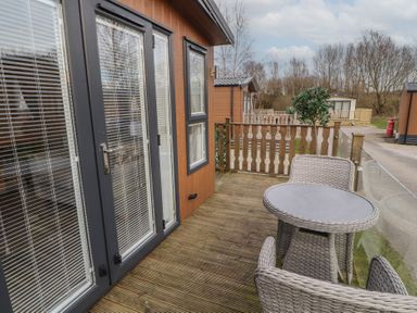 An outdoor wooden deck with a round table and two wicker chairs outside a building with glass doors and windows at 24 Sherwood in Carnforth