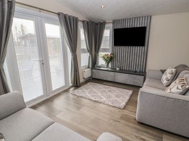 A living room with grey sofas a wall-mounted television grey curtains and a rug at 24 Sherwood in Carnforth