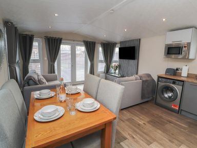 A dining table set with plates and glasses next to a living area with sofas and a mounted TV at 24 Sherwood in Carnforth