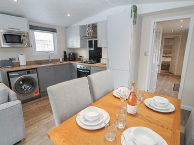 A kitchen with grey and white cabinets a wooden dining table set with plates bowls glasses and a bottle at 24 Sherwood in Carnforth