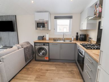A kitchen with washing machine microwave toaster and stove next to a living room with a couch at 24 Sherwood in Carnforth