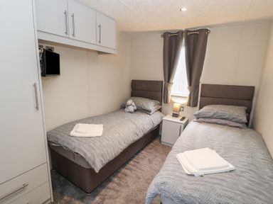 A bedroom with two single beds a nightstand a lamp a television and curtains at 24 Sherwood in Carnforth