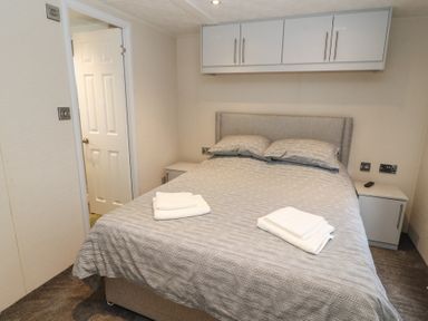 A bedroom with a double bed two bedside tables overhead cabinets and folded towels on the bed at 24 Sherwood in Carnforth