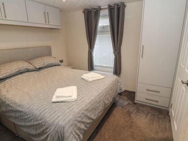A bedroom with a double bed with towels on it a window with curtains and a wardrobe at 24 Sherwood in Carnforth