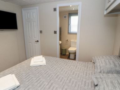 A bedroom with a bed and folded towels with a door leading to a bathroom with a toilet and window at 24 Sherwood in Carnforth