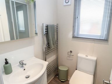 A bathroom with a sink and soap dispenser a towel rack with a towel a toilet a waste bin and a window with blinds at 24 Sherwood in Carnforth