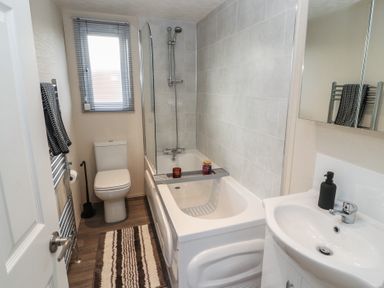 A bathroom with a bathtub a shower a toilet a sink a towel on a radiator and a striped rug at 24 Sherwood in Carnforth