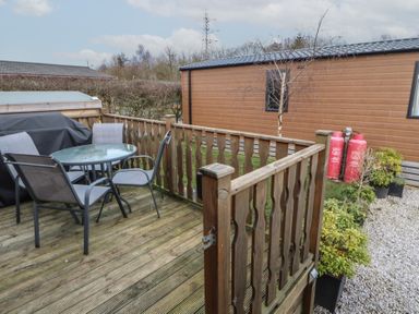 A wooden deck with a glass table and chairs next to a mobile home and garden at 24 Sherwood in Carnforth