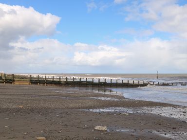 A pebble and sand beach with wooden groynes extending into the sea under a partly cloudy sky at Church View in Atwick