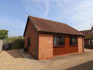 A single story house with brick and wood panel exterior and a tiled roof surrounded by a gravel driveway at Church View in Atwick