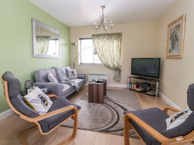A living room with two armchairs, a sofa, a coffee table, a television, a standing lamp and a window with curtains at Church View in Atwick