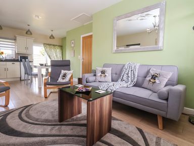 A living room with grey sofa and armchair with bee cushions and a wooden coffee table at Church View in Atwick