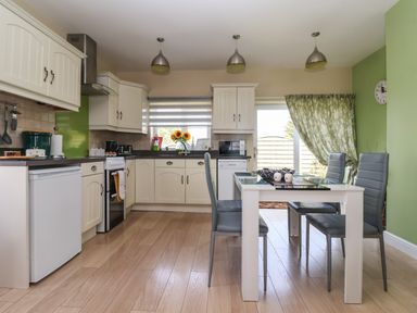 A kitchen with white cabinets a dining table with four chairs and green walls at Church View in Atwick