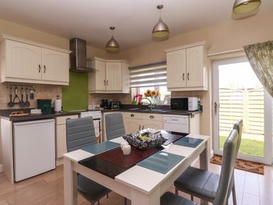 A kitchen with white cabinets a dining table with four chairs and a glass door leading outside at Church View in Atwick