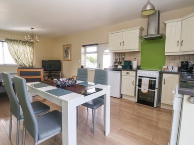 A kitchen and dining area with a white dining table, four grey chairs, white cabinets, a stove with a green backsplash, and a television in the corner at Church View in Atwick